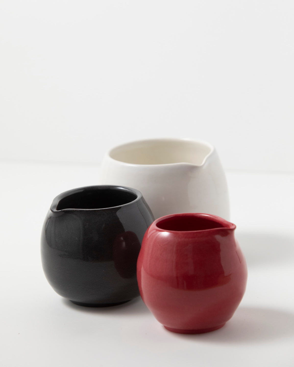 Three small ceramic pitchers in glossy black, white, and red